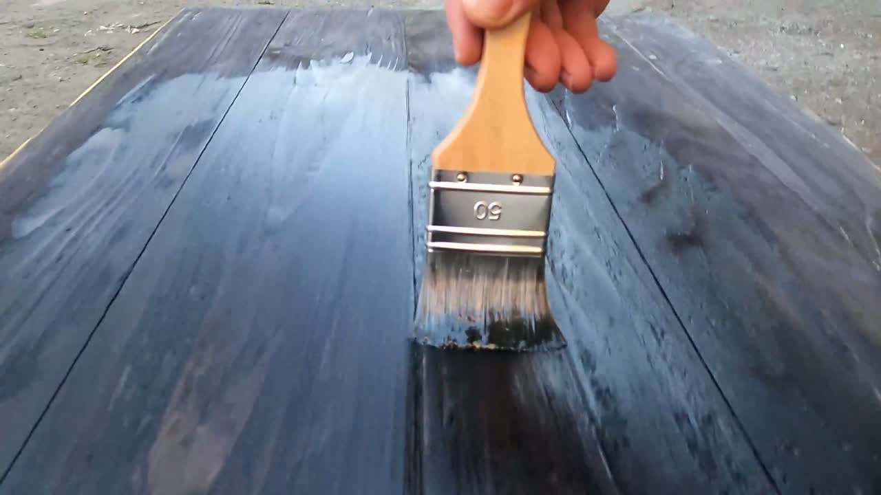 Breiter Pinsel zieht Lasur über Holz